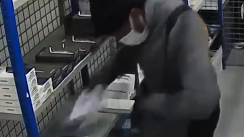 A CCTV image of a man shovelling phones into a bag.