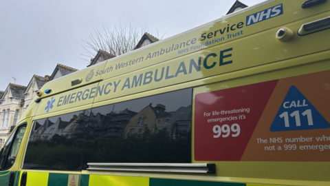 The side of a South Western ambulance. It looks as though it is parked on a residential road.