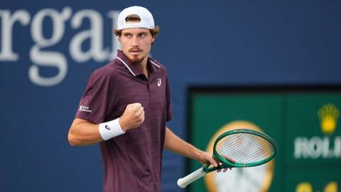 Toby Samuel clenches his fist while on court holding a green tennis racquet