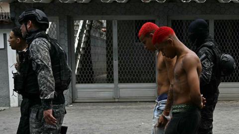 Police officers escort suspects arrested during the Operacao Contencao (Operation Containment) out of the Vila Cruzeiro favela, in the Penha complex, in Rio de Janeiro, Brazil, on October 28, 2025.