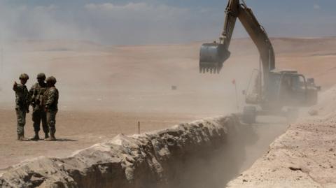 Members of the Chilean army stand near a trench dug by heavy machinery in the desert.