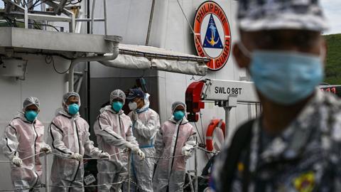 People wearing protective suits and masks aboard a coast guard ship