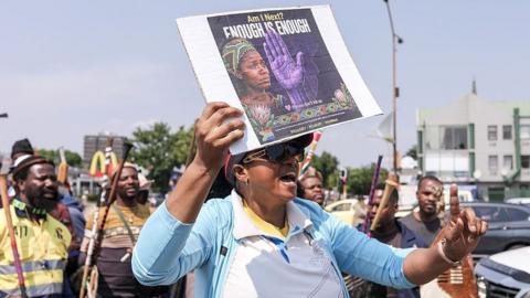 A woman holds up an anti-abuse poster as she joins a protest in South Africa