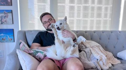 Denis pictured with a dog on a grey sofa