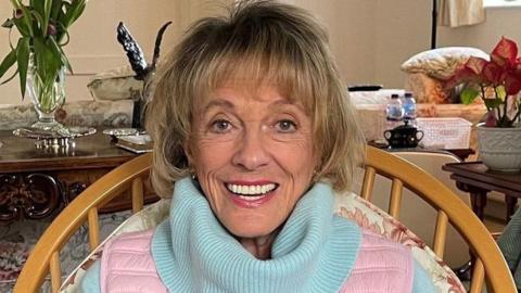Esther Rantzen photographed towards the end of her life. She is at home looking directly into camera and smiling.