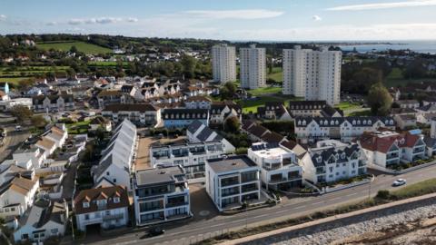 An aerial image of St Clements in Jersey. It features a seafront and multi-storey properties. In the background is the sea and green fields.