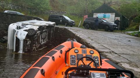 A white campervan lying on its side beside a slipway