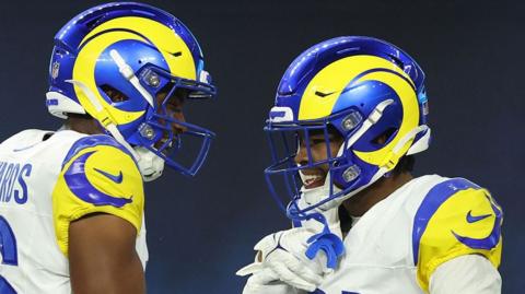 Two men in American football helmets smile and clasp hands