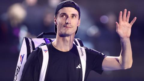 British tennis player Joe Salisbury waving with a tennis bag on his shoulder