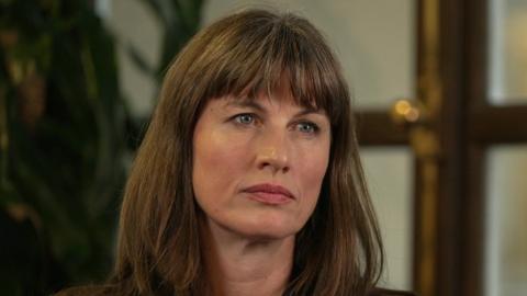 A woman with long, brown hair. She has blue eyes and is looking past the camera.