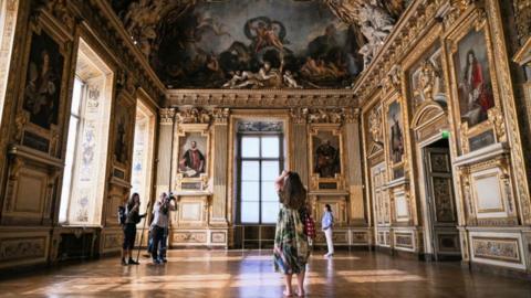 A visitor takes a picture in the Apollo Gallery during its reopening at the Louvre Museum