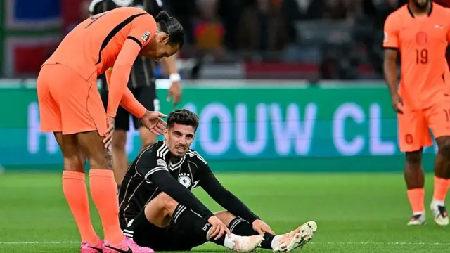 Kai Havertz sits on the pitch grimacing as Virgil van Dijk checks on him