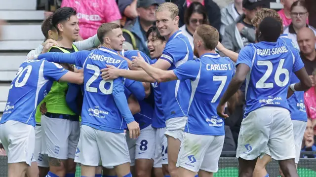 Birmingham City players, wearing their blue shirt and white shorts, gather in a huddle after scoring a goal against Derby County