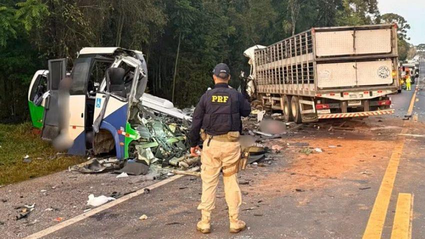 An officer with Brazil's Federal Highway Police looks at the wreckage of a minibus and a truck which collided on the BR-373 highway in the southern Brazilian state of Parana. Both vehicles have veered off the road. The minibus is almost completely destroyed, with broken glass and pieces of metal scattered on the road. The rear of the truck is showing less damage, the front appears damaged but cannot be made out clearly on the photo.