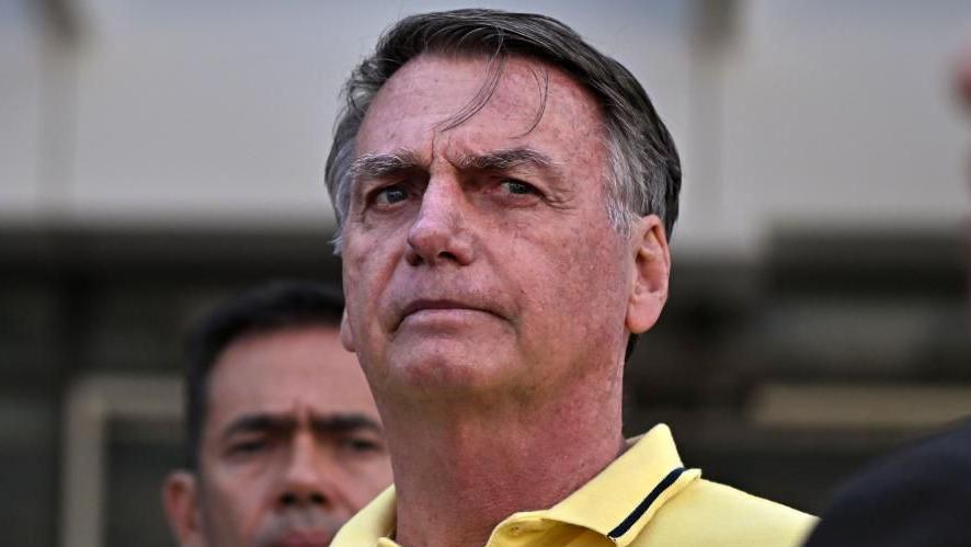 Jair Bolsonaro leaves hospital on 16 August. He is wearing a pale yellow polo shirt. A strand of hair has fallen onto his forehead.
