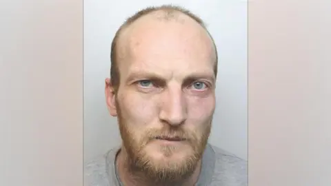 Cheshire Constabulary A police mugshot of John Whitfield, who has blue eyes, receding hair and a ginger beard