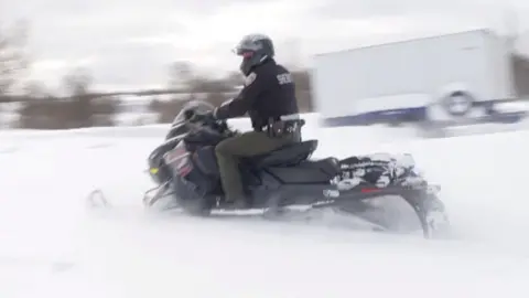 A policeman rides on a snowmobile.