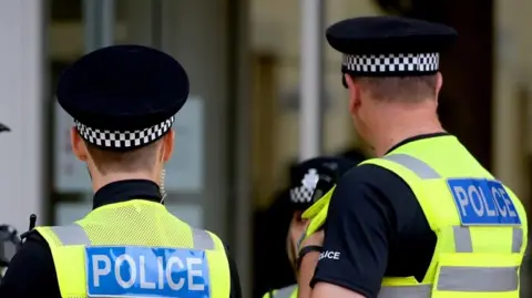 Two police officers with their backs to the camera, dressed in high visibility jackets and black hats.