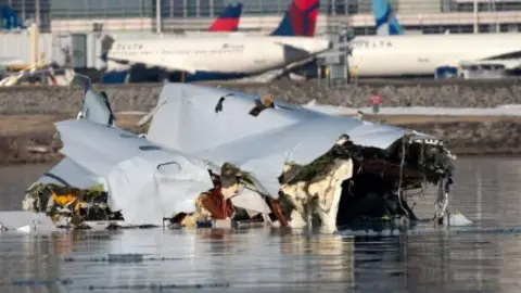 The wreckage of the American Airlines plane in the Potomac River, with two parked aircraft visible in the background
