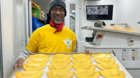 'Baker’ smiles as he holds up a tray of patties