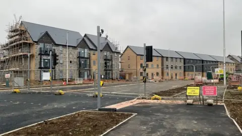 A new housing estate being built with some part finished houses and some that are complete. They are pale brick with some black sections and slate grey roofs.