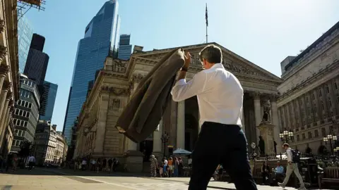 A commuter carries his jacket on a sunny day in the City of London