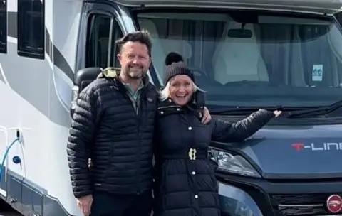 Couple in black coats standing in front of their motorhome. 