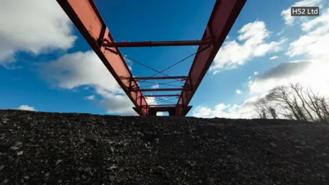 Part of the metal frame of a bridge being moved over the edge of a stony embankment