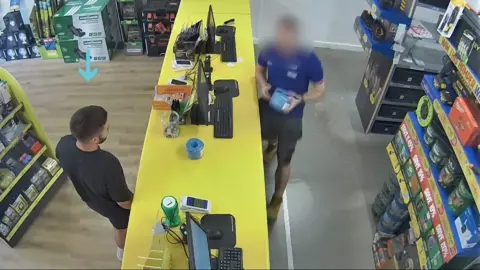 Kyle Clifford at the yellow counter in a Toolstation store, with a shop assistant on the other side of the counter