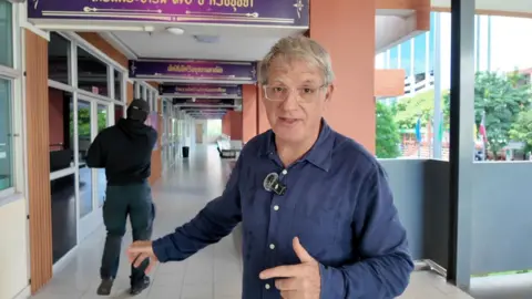 BBC correspondent Jonathan Head and a man dressed in black standing in a school corridor in Bangkok