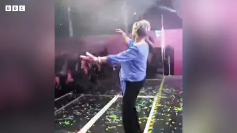 Anne dances on stage in a purple jumper and black trousers