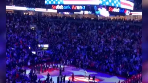 A basketball court with players and fans is pictured.