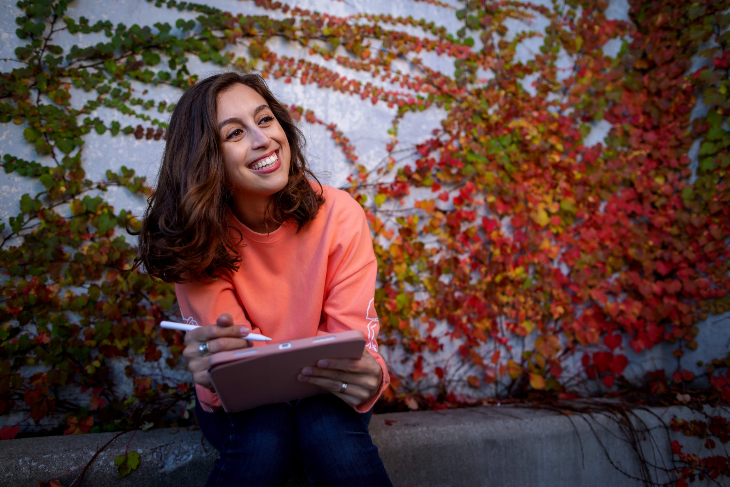 Author Cassidy sitting in front of a vine-covered wall, working on her tablet