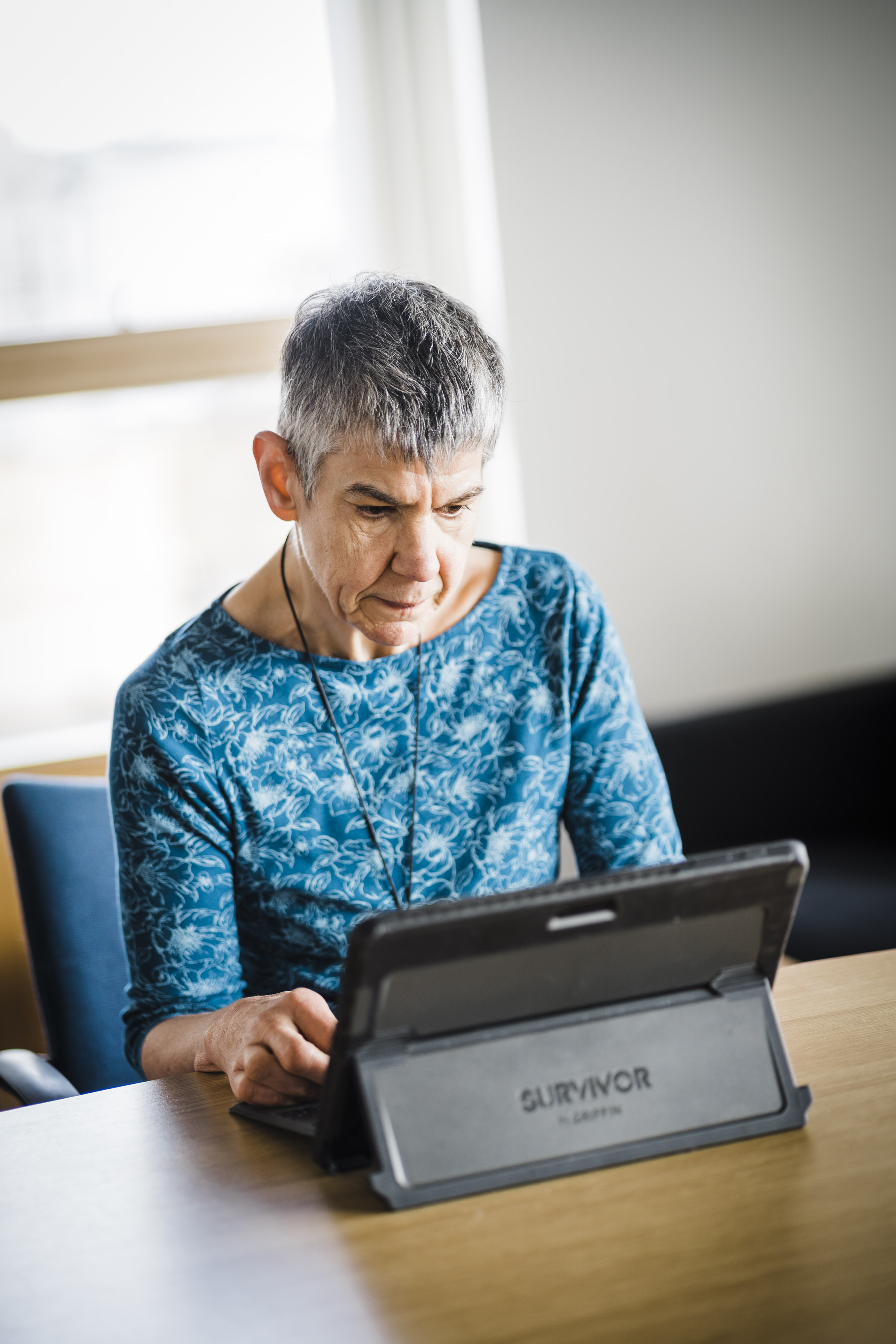 Wearing a blue shirt, Annalu sits at a wooden table working on her laptop.