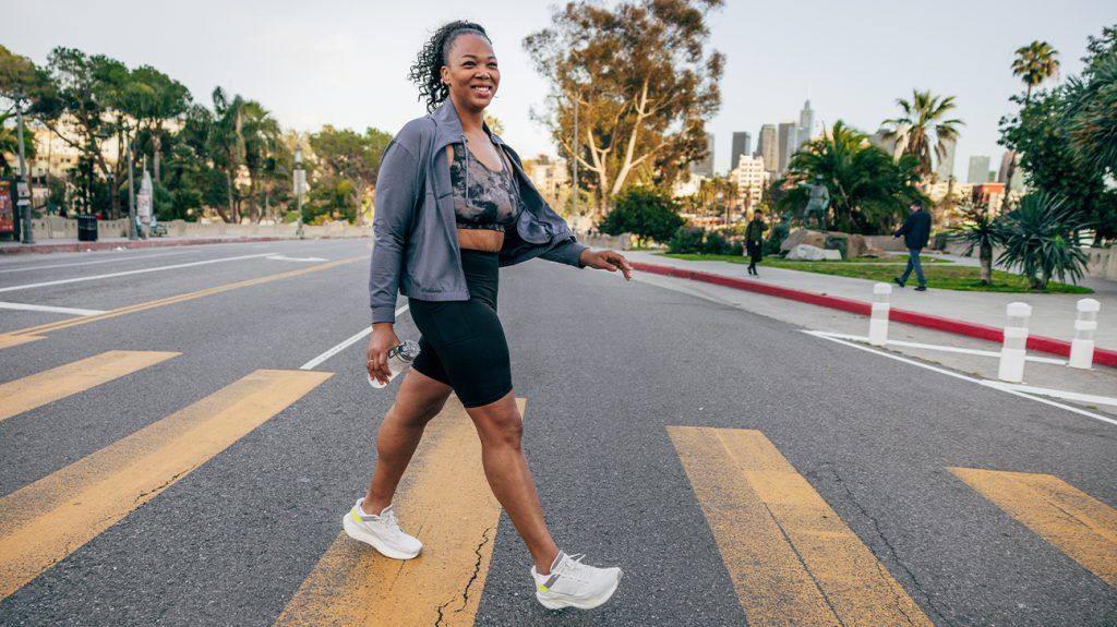 A woman wearing athleisure walks on a side walk while smiling