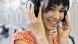 A woman an orange flower dress smiling about what she is hearing via her headphones A woman an orange flower dress smiling about what she is hearing via her headphones