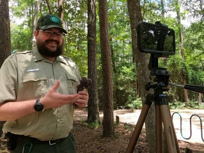 Distance Learning - John Herron Park ranger recording a program on a tablet on a tripod under tall trees.