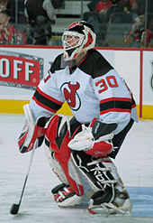 A hockey goaltender stands in front of his net with his glove and stick ready to make a save.