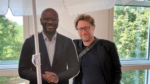 Ein Pappaufsteller des Politikers Armand Zorn und ein Mann unter einem Sonnenschirm